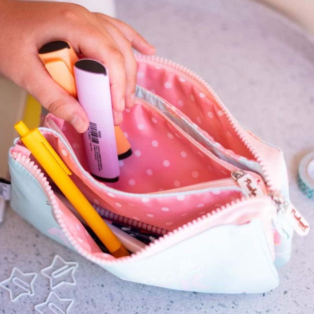 Eine Hand legt Textmarker in eine pastellfarbene Federtasche mit rosa Pünktchenfutter.