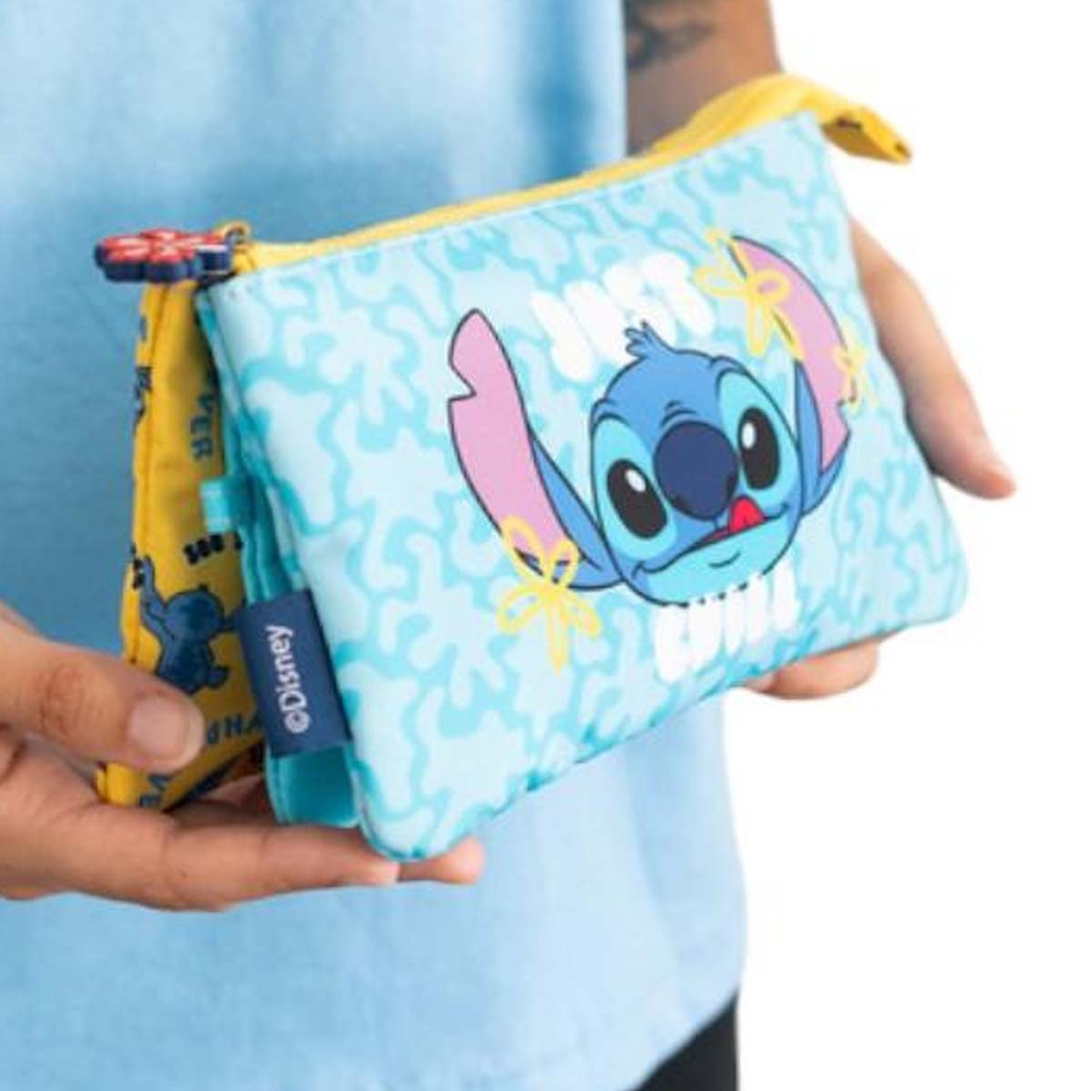 Eine Person hält zwei bunte Beutel mit Stitch-Motiv. Einer ist hellblau mit Stitch, der andere gelb.