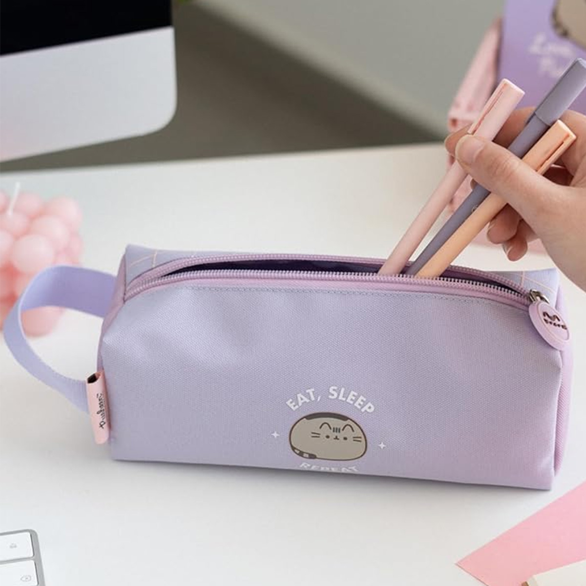 Eine lavendelfarbene Federtasche mit einem Katzenmotiv und der Aufschrift "Eat, Sleep, Repeat".