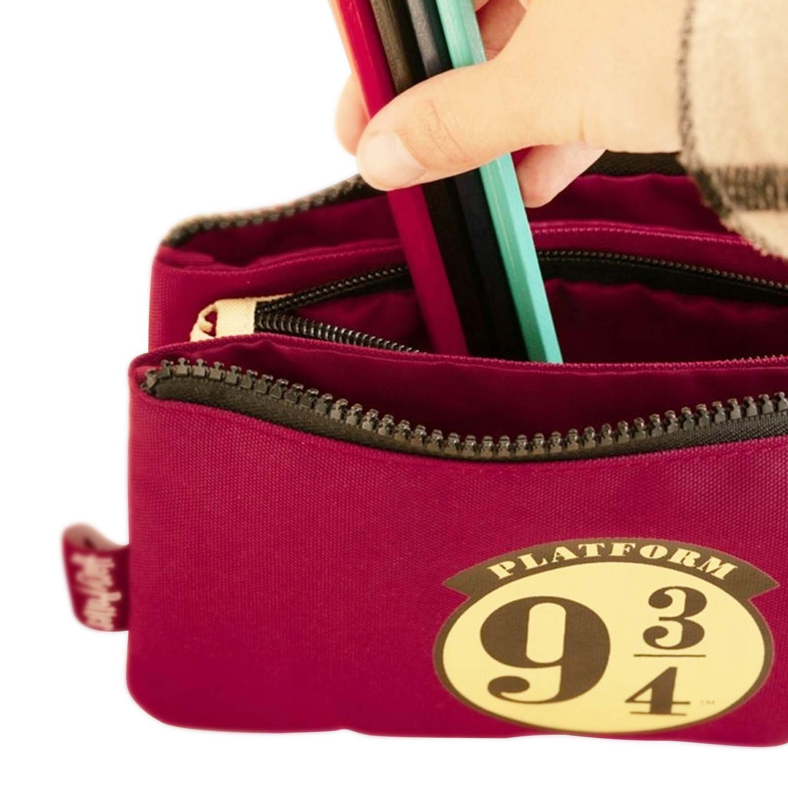 Eine Hand steckt rote, schwarze und türkise Stifte in eine burgunderrote Tasche mit der Aufschrift „Platform 9 ¾“.