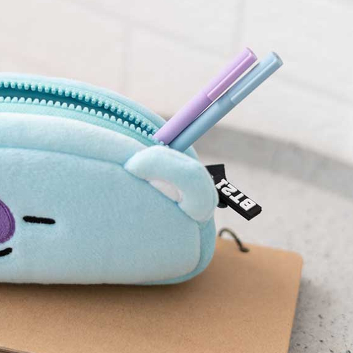 Eine hellblaue Plüschtasche mit zwei Stiften, lila und blau, steckt heraus.