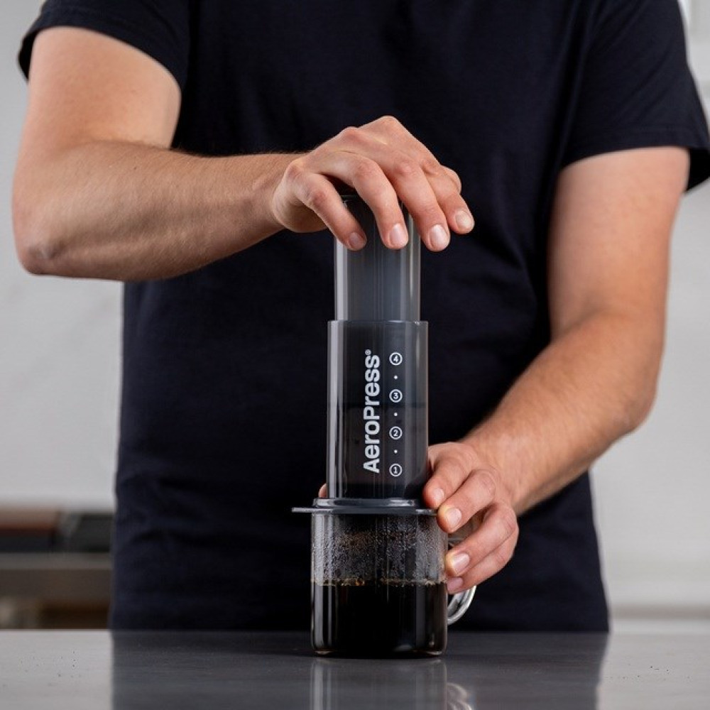 Una persona usa una caffettiera AeroPress per preparare il caffè in una tazza di vetro.