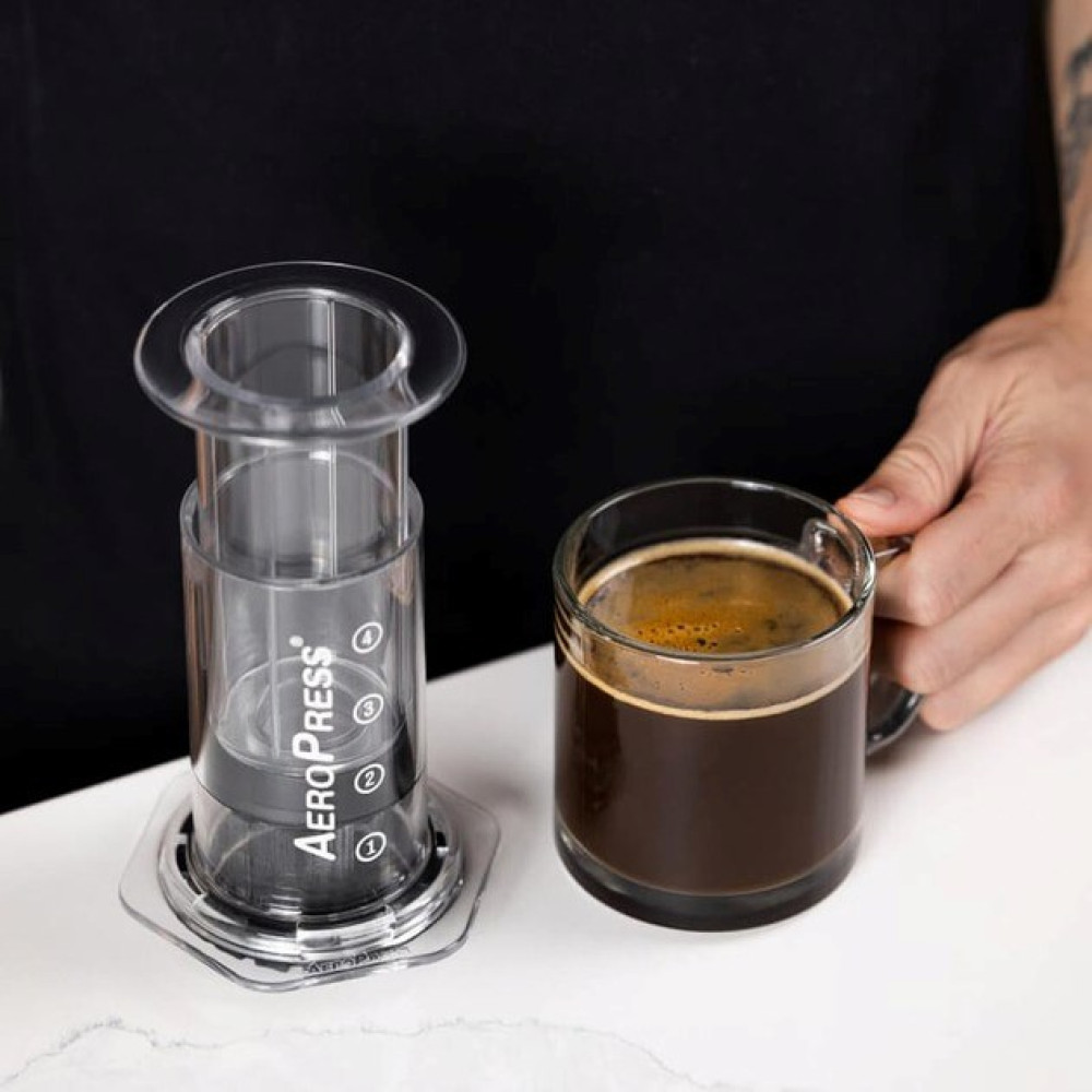 Ekspres AeroPress i kubek kawy obok siebie.