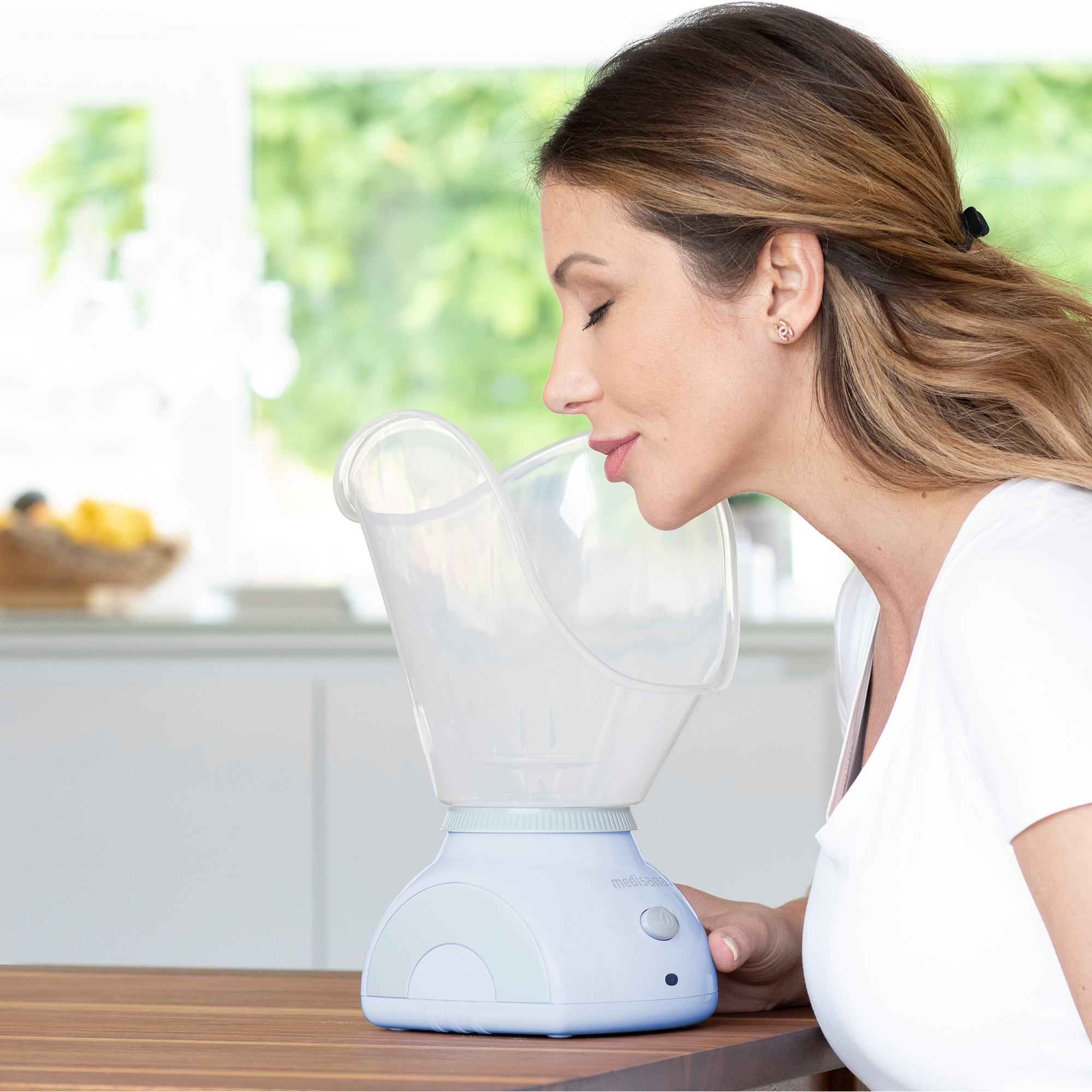 Eine Frau inhaliert Dampf aus einem Inhalator auf einem Holztisch.
