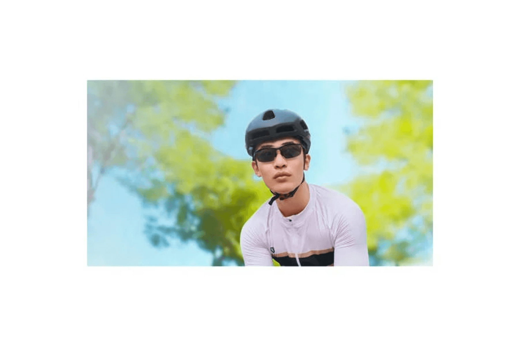 Un hombre con casco y gafas de sol mira hacia adelante, con árboles al fondo.