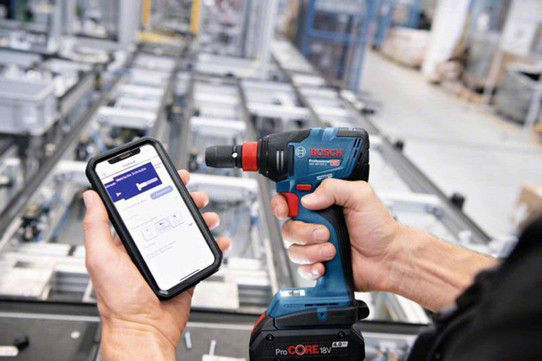 Person hält Smartphone mit Schrauben-App & Bosch Akkuschrauber in Fabrik.