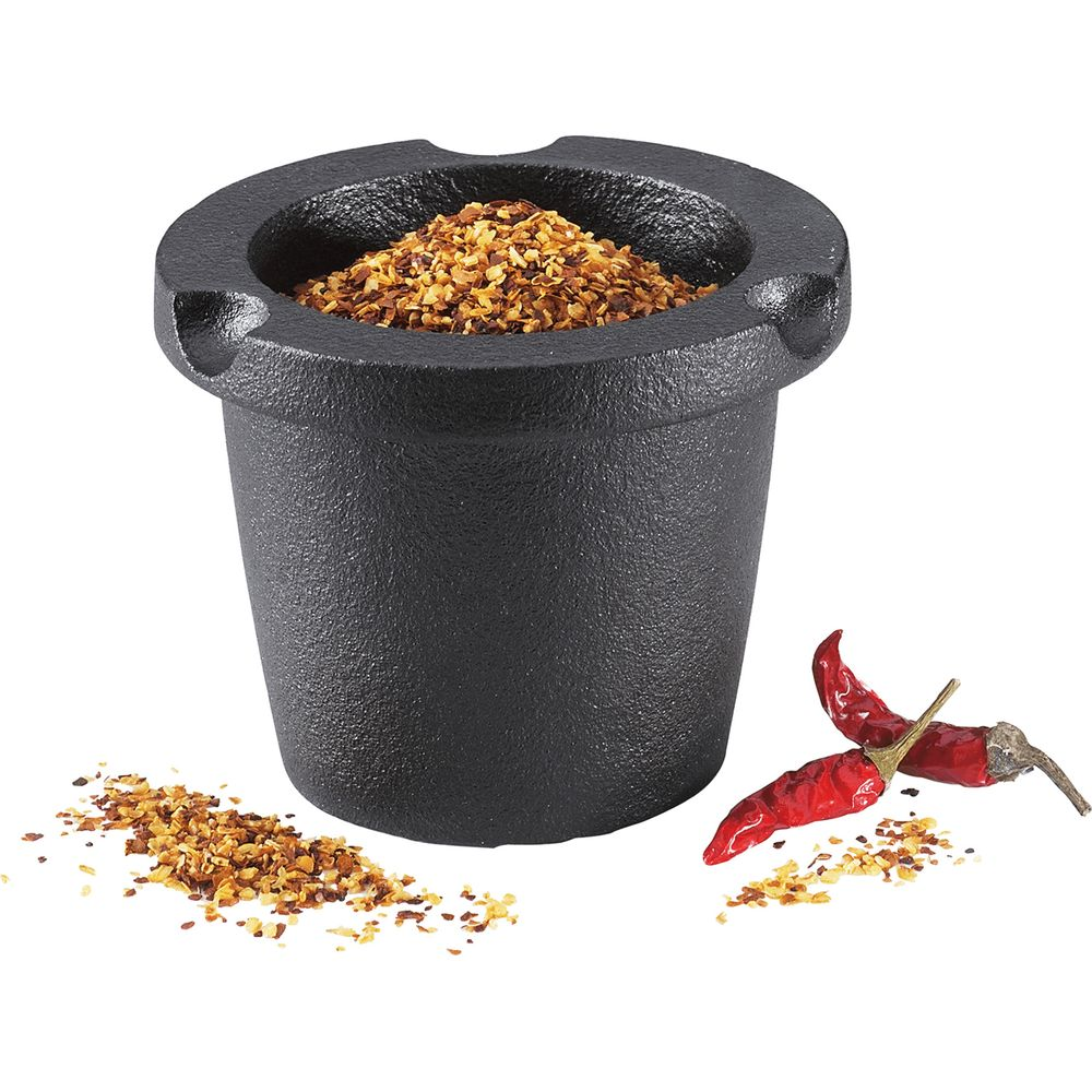 Schwarzer Mörser gefüllt mit Chiliflocken, daneben zwei getrocknete Chilis.