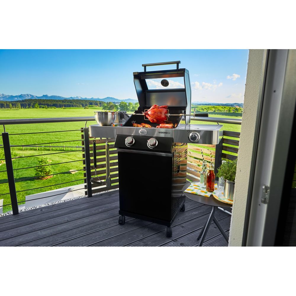 Una griglia con pollo arrosto su un balcone, con vista su campi verdi e montagne.