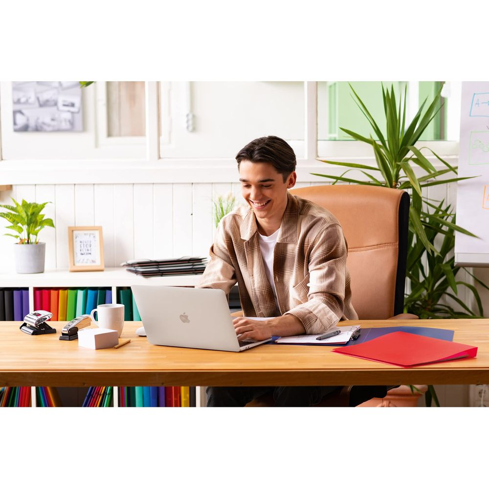 Ein junger Mann sitzt an einem Schreibtisch und arbeitet an einem Laptop. Im Hintergrund sind Pflanzen und Aktenordner.