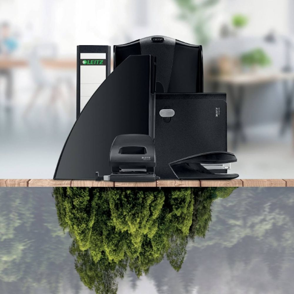 Schwarze Leitz Büromaterialien auf einem Holztisch mit Spiegelung von Bäumen.