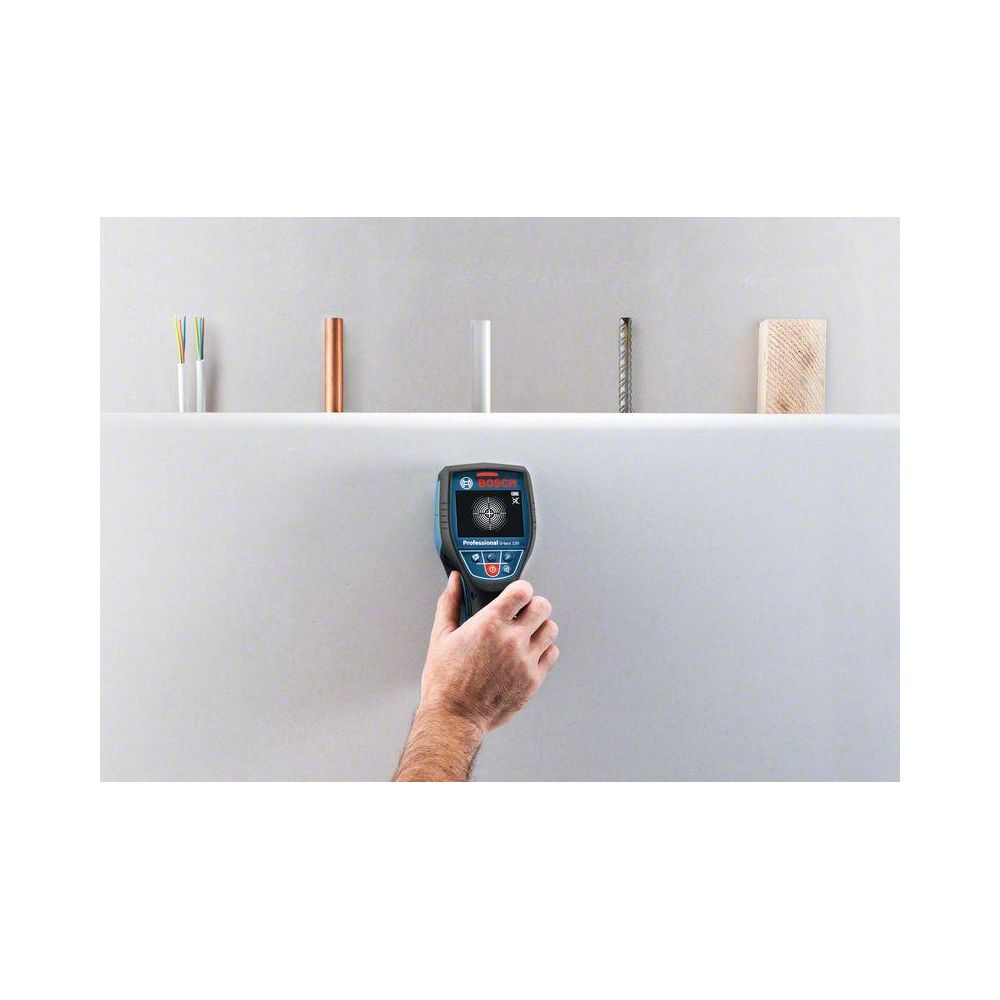 Hand hält Bosch-Detektor an Wand mit Drähten, Kupfer und Holzproben.