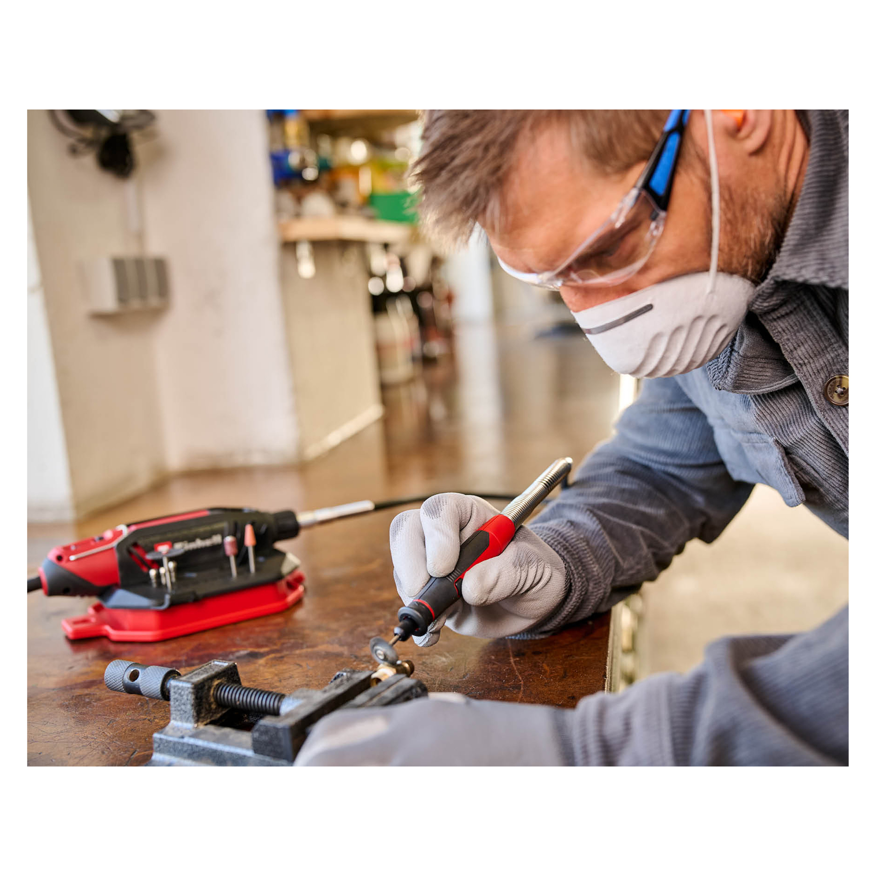 Mann mit Schutzbrille und Maske arbeitet mit einem Schleifgerät an einem Gegenstand.