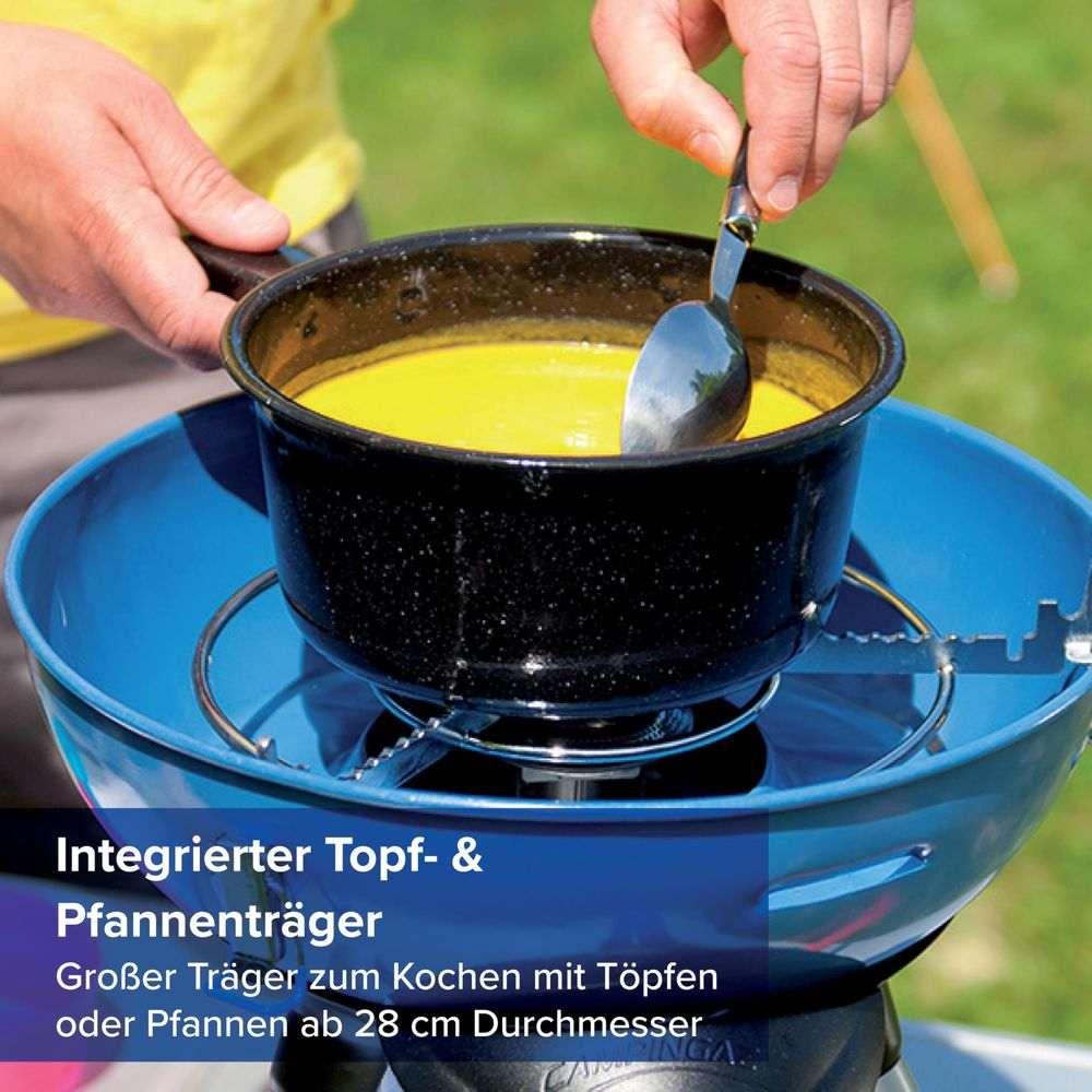 Gelbe Suppe wird in einem Topf auf einem blauen Campingkocher mit einem Löffel umgerührt.
