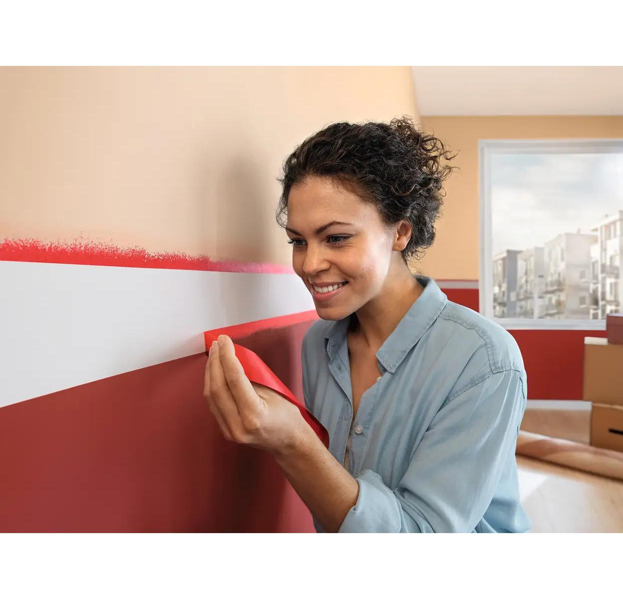 Eine Frau entfernt rotes Klebeband von einer Wand mit zwei Farbbereichen.