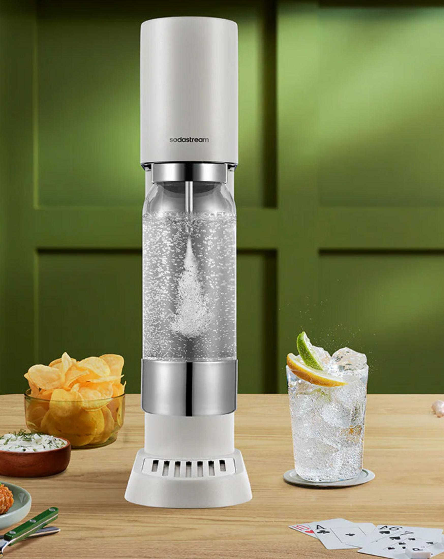 Ein Wassersprudler steht auf einem Holztisch neben Chips und einem Getränk.
