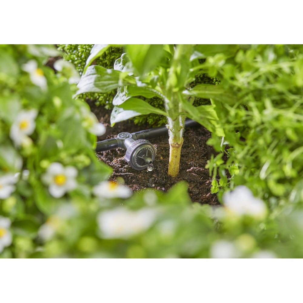 Ein Tropfer in einem Gartenbeet mit Pflanzen und Blumen, der Wasser auf den Boden tropft.
