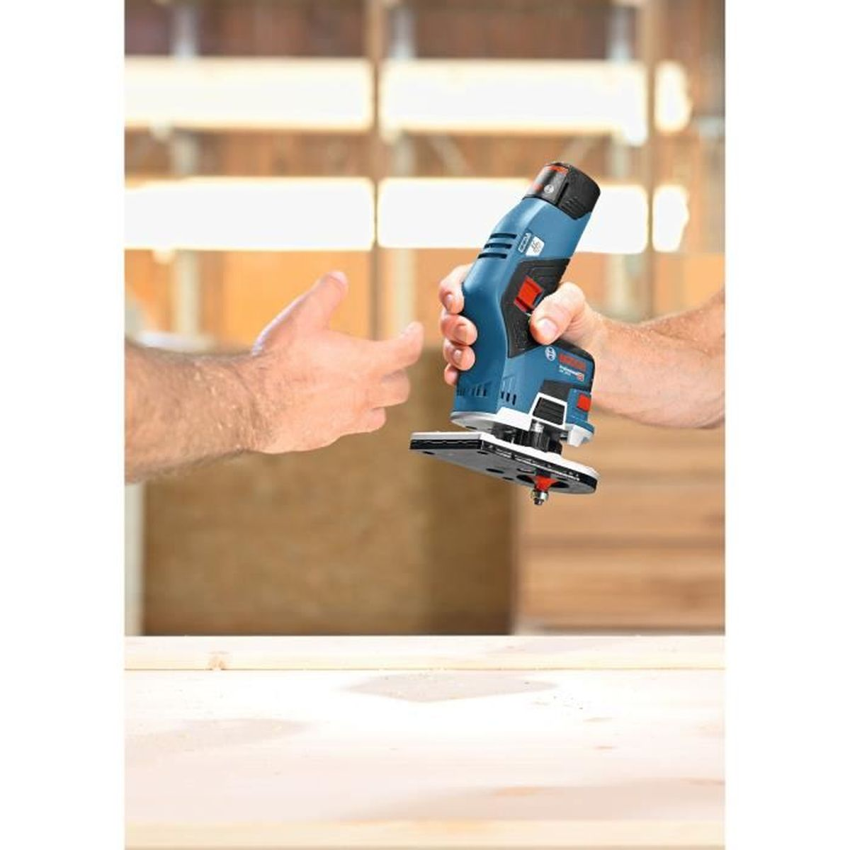 Eine Hand hält einen blauen Bosch-Trimmer über Holz.