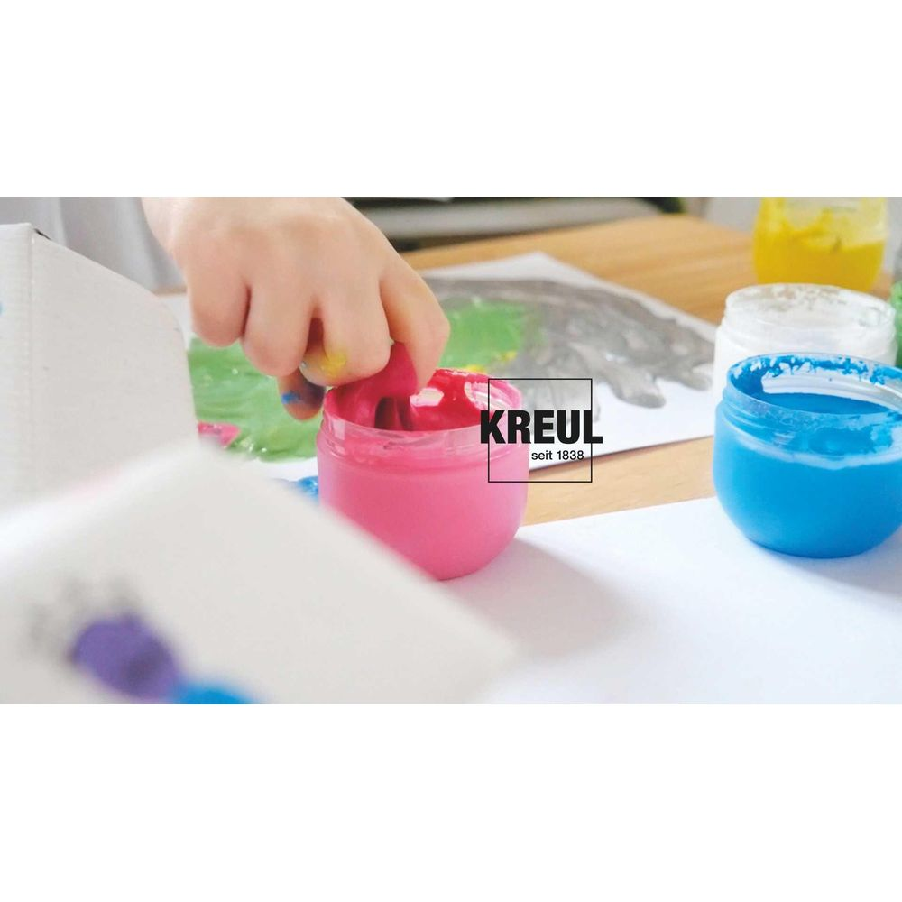 Ein Kind taucht seinen Finger in rosa Farbe. Daneben stehen Behälter mit blauer und weißer Farbe.