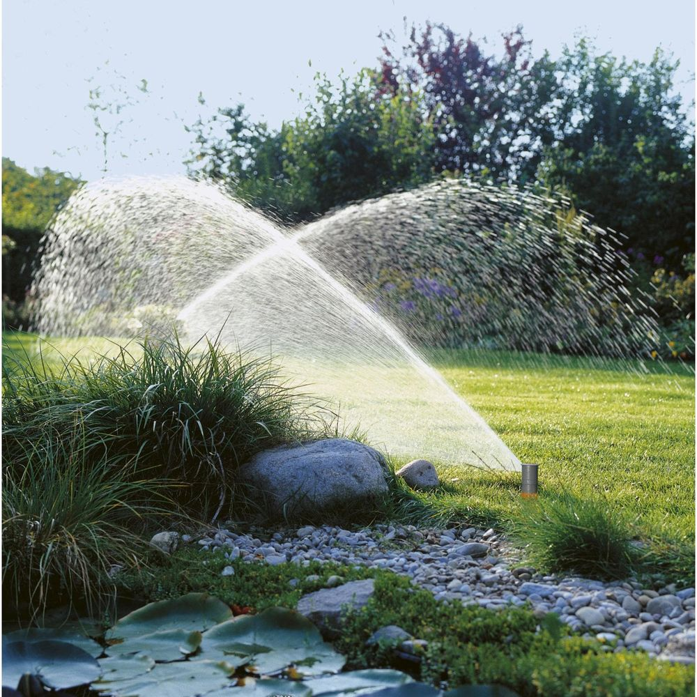 Un irrigatore per prato annaffia un giardino con stagno e alberi.