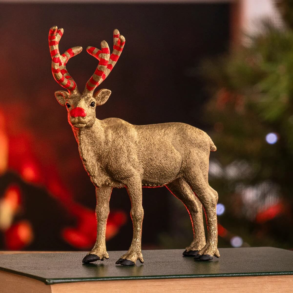 Figurine de renne dorée avec nez rouge et bois rayés.