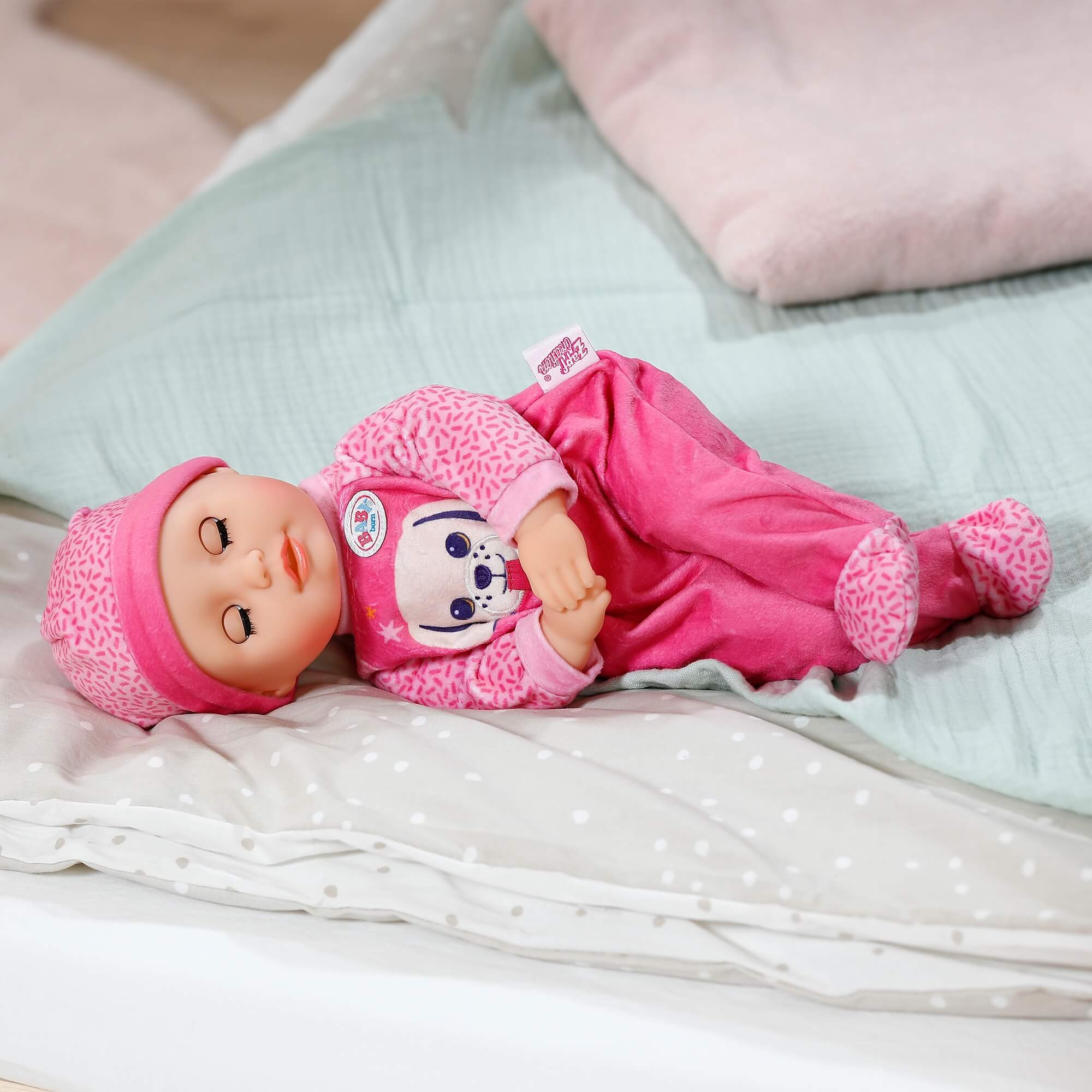 Ein rosa Baby-Strampler mit Hundedekor liegt auf Bettwäsche.