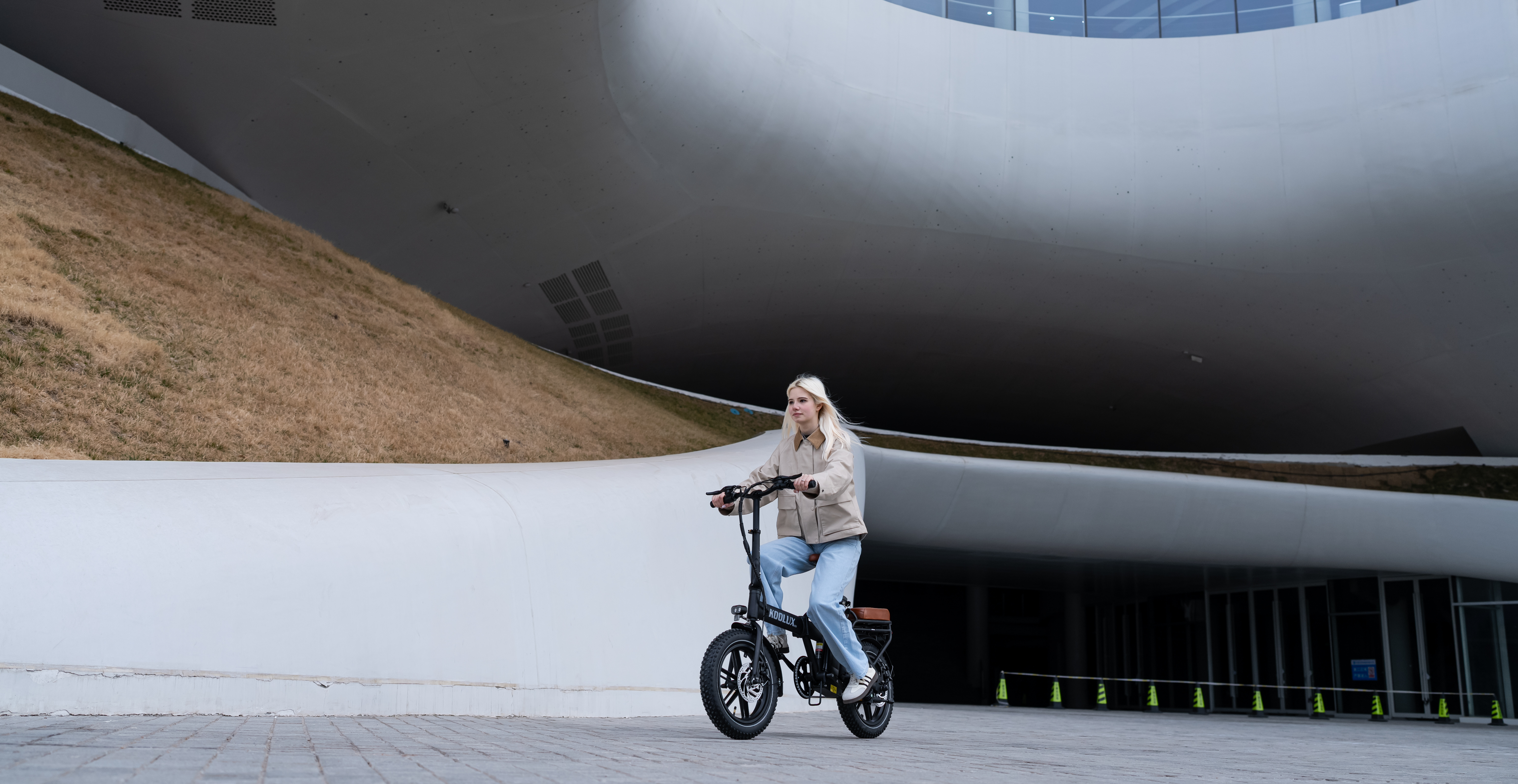 Una mujer monta una e-bike negra frente a un edificio moderno de líneas curvas.