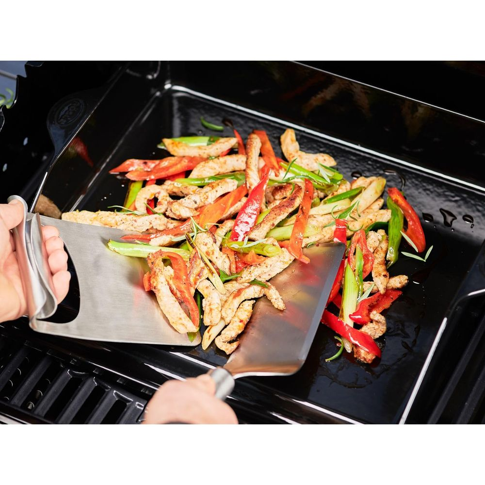 Fleischstreifen mit Paprika und Lauchzwiebeln werden auf einem Grillblech mit zwei Pfannenwendern gewendet.