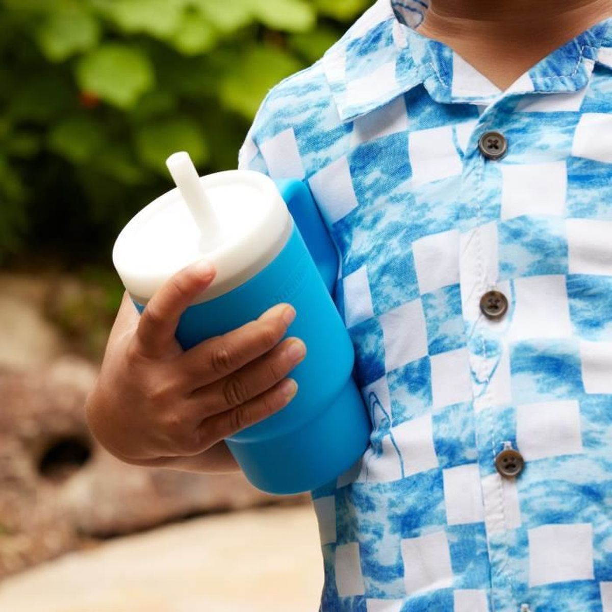 Ein Kind in einem blau-weiß karierten Hemd hält einen blauen Becher mit weißem Strohhalm.