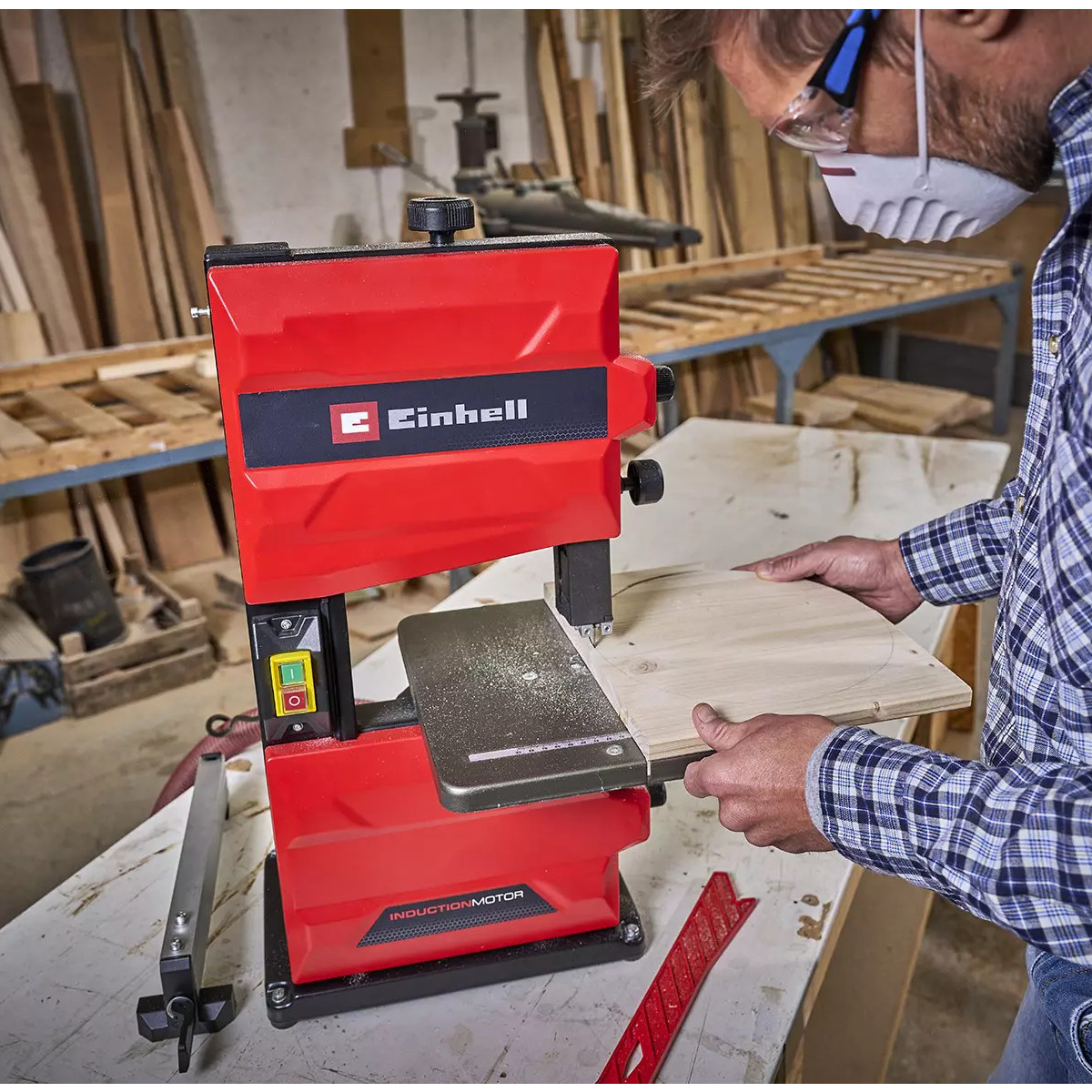 Mann schneidet Holz mit roter Einhell Bandsäge. Werkstatt im Hintergrund.