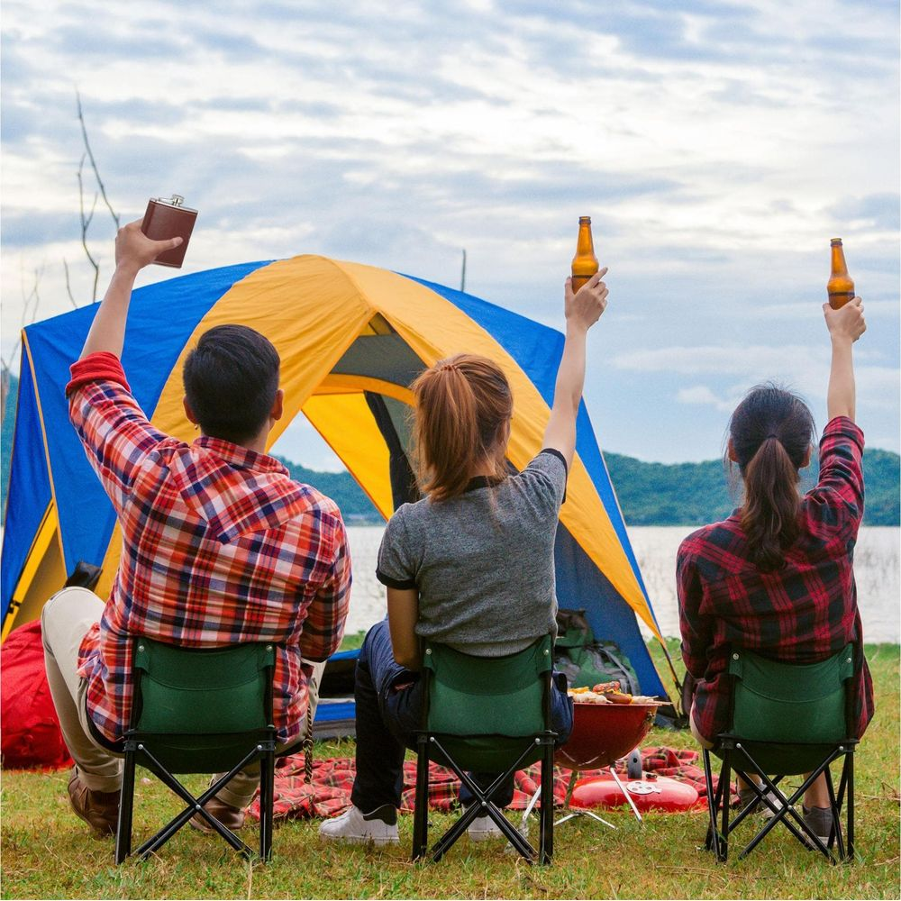 Drei Freunde feiern beim Camping mit Getränken vor einem Zelt am See.