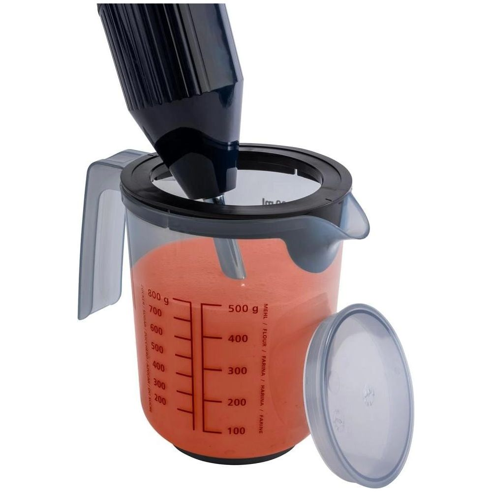 Ein schwarzer Stabmixer mischt orangefarbene Flüssigkeit in einem durchsichtigen Messbecher mit Deckel.
