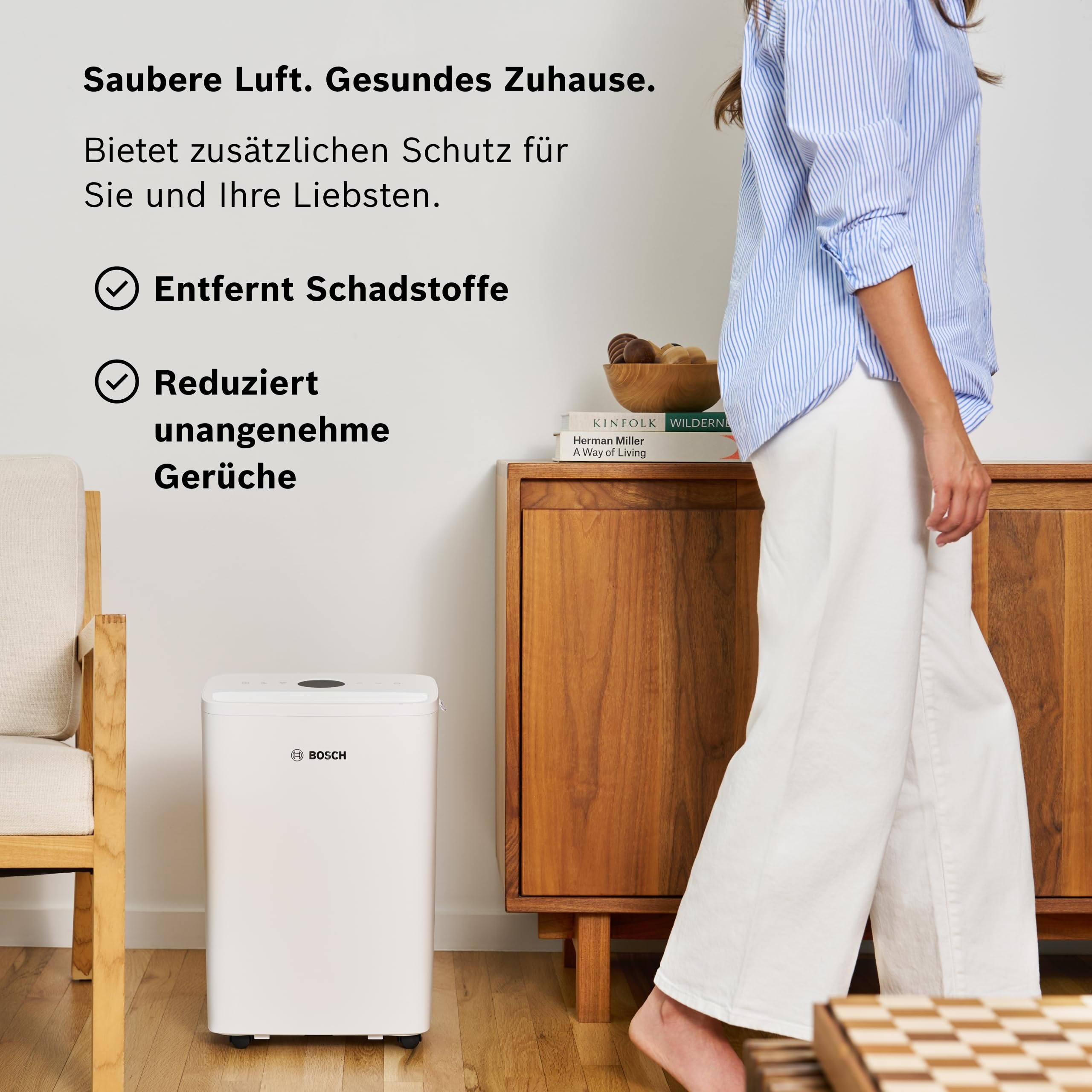 Ein weißer Bosch Luftreiniger steht neben einem Sessel und einem Holzschrank.
