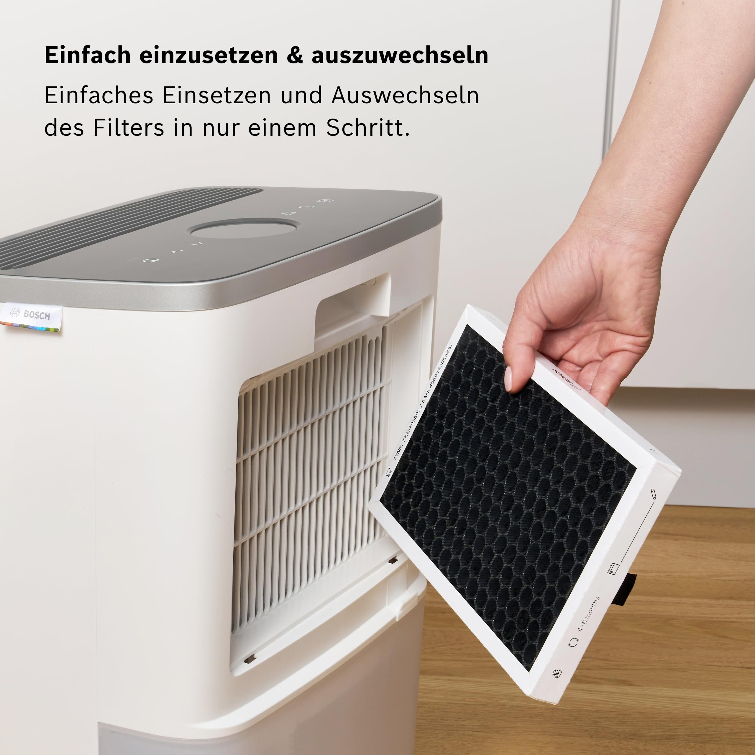 Eine Hand tauscht einen schwarzen Filter in einem weißen Luftreiniger aus.