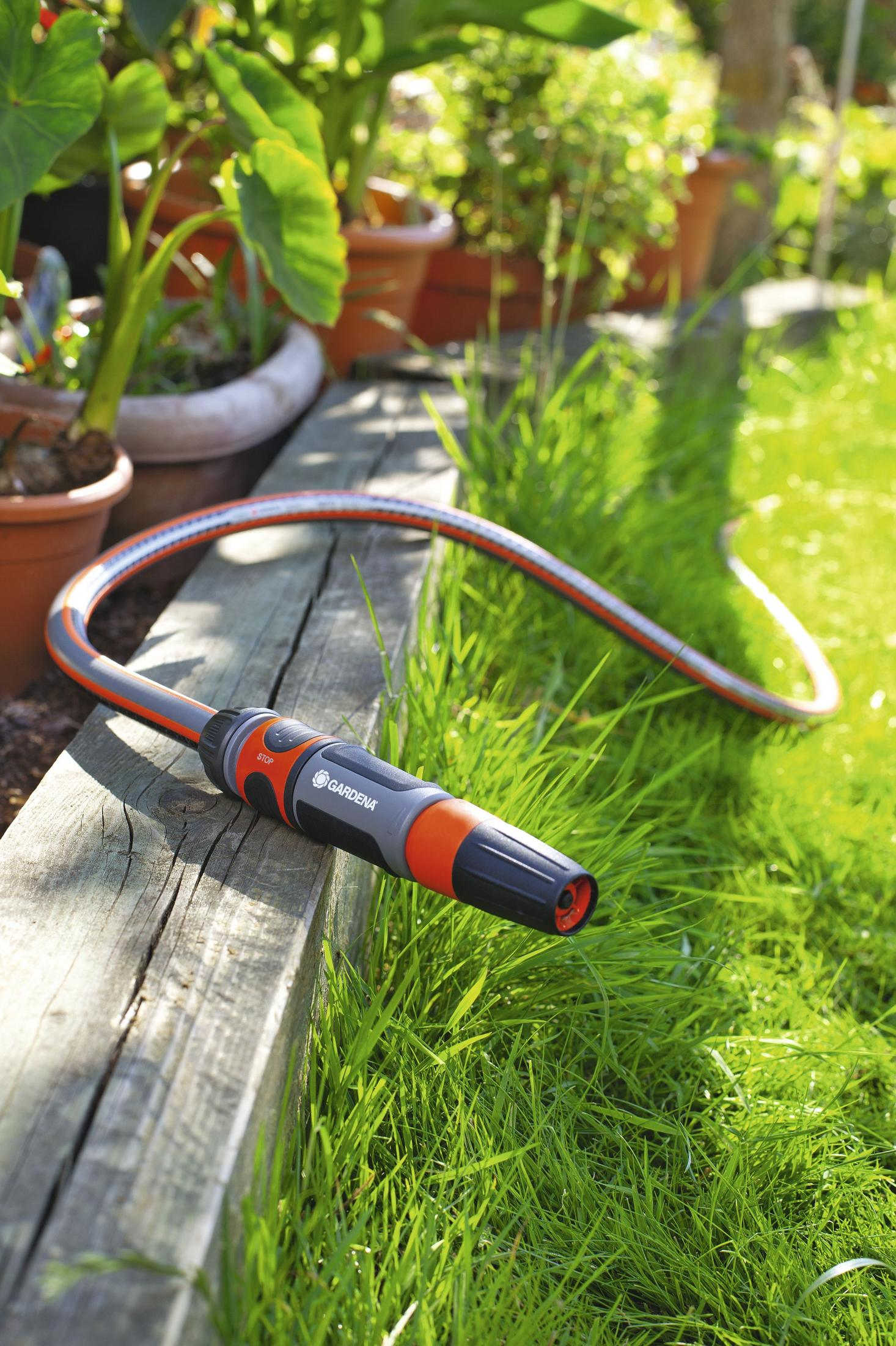 Gartenschlauch mit Sprühkopf auf Holzbank neben grünem Gras