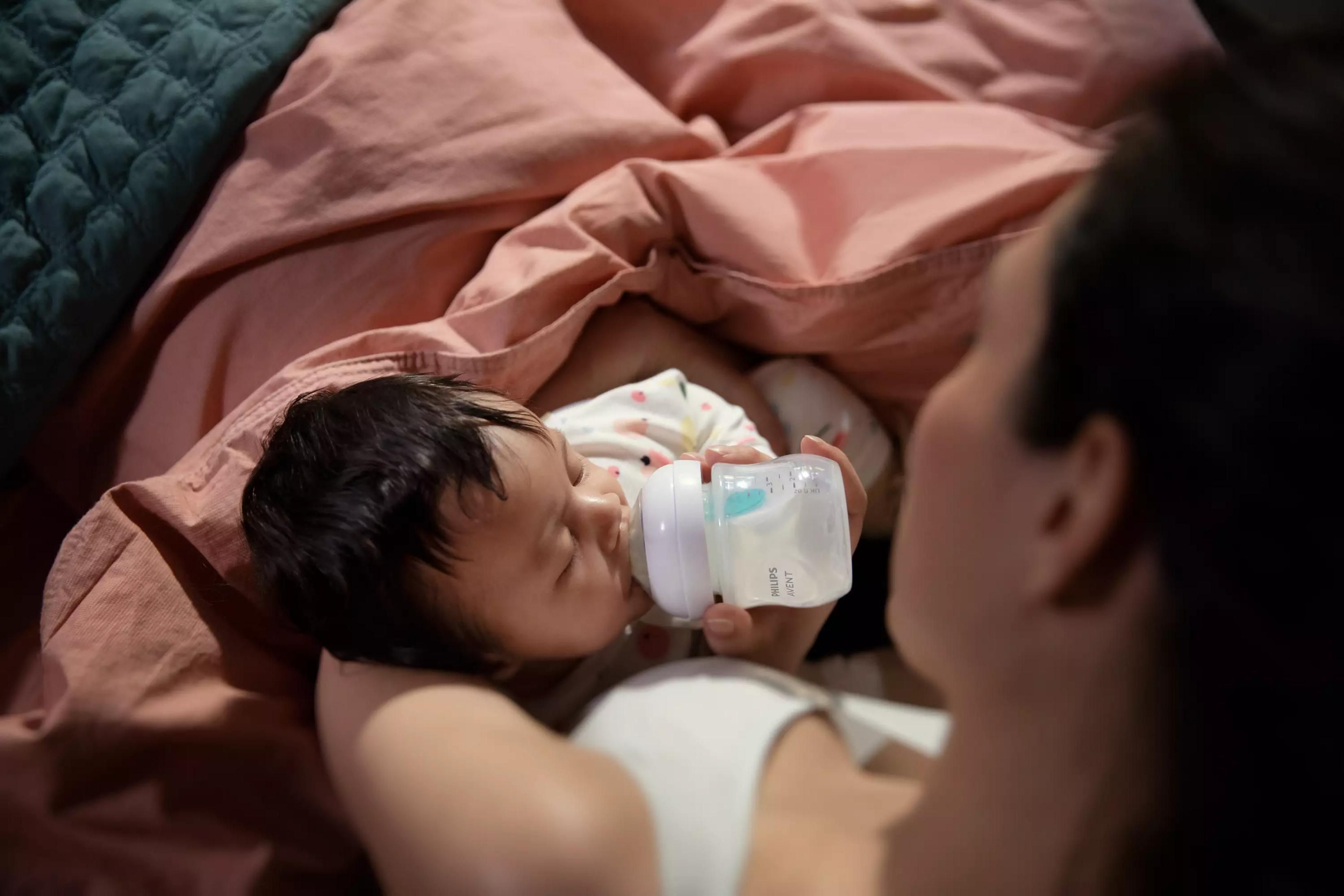 Ein Baby trinkt aus einer Flasche, umgeben von Decken in Rosé- und Grüntönen.