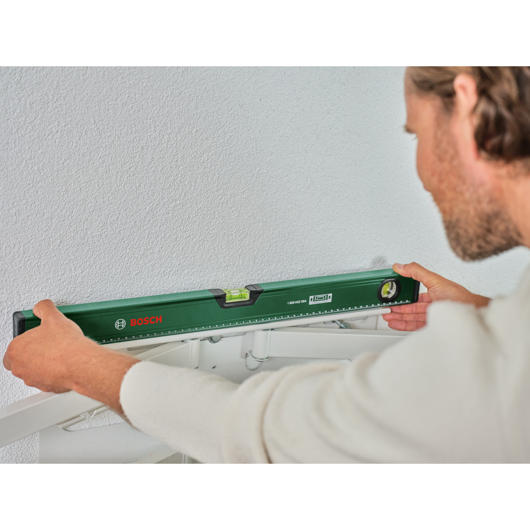 Mann hält Wasserwaage mit Bosch-Logo an eine weiße Wand, um sie auszurichten.