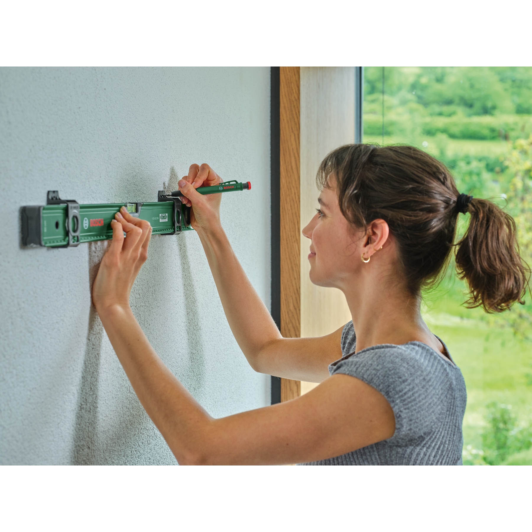 Eine Frau benutzt ein grünes Bosch-Wasserwaage-Werkzeug an einer Wand.