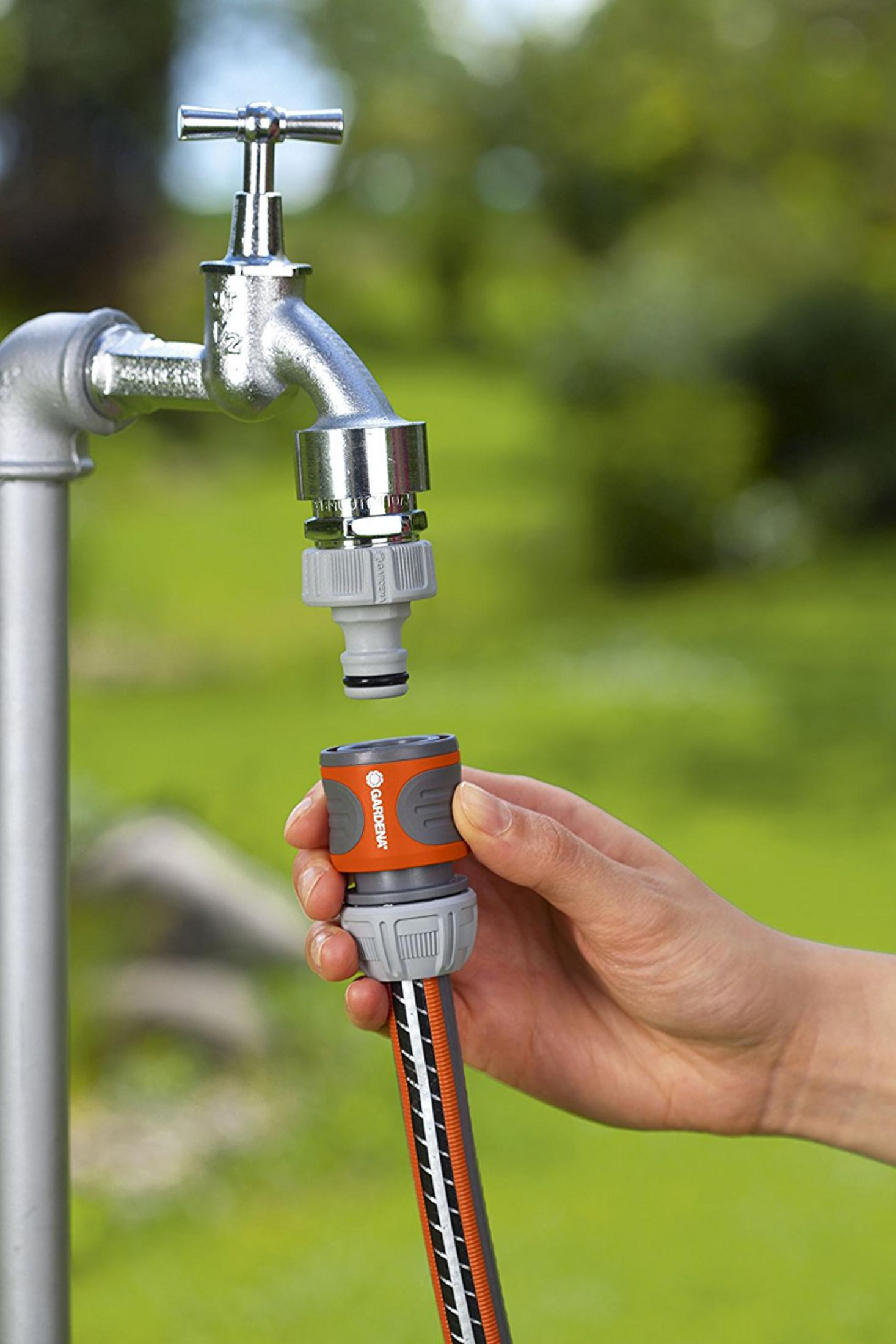 Eine Hand hält einen Gartenschlauchanschluss an einem Wasserhahn.