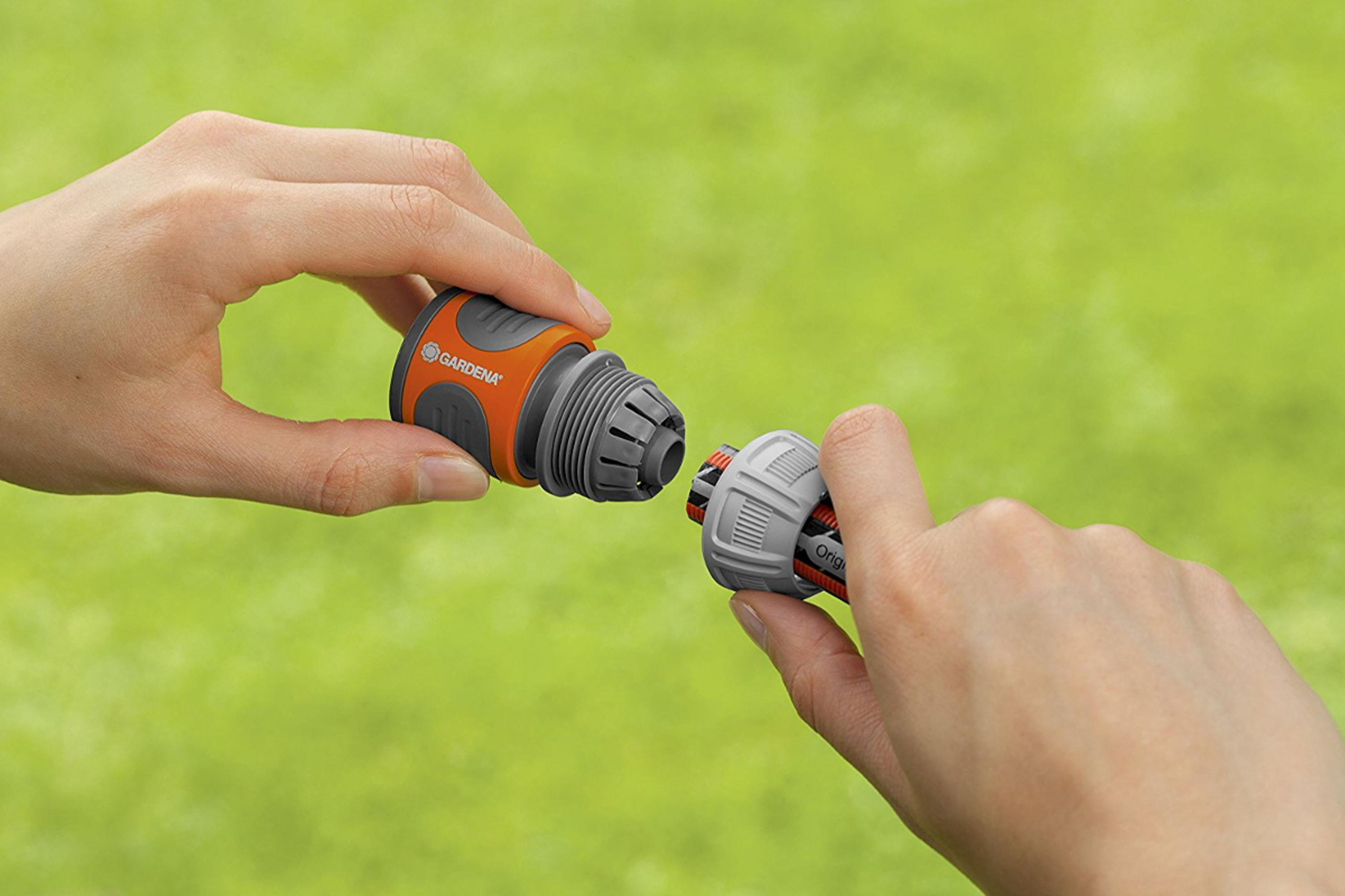 Zwei Hände verbinden einen orange-grauen Gartenschlauchanschluss.