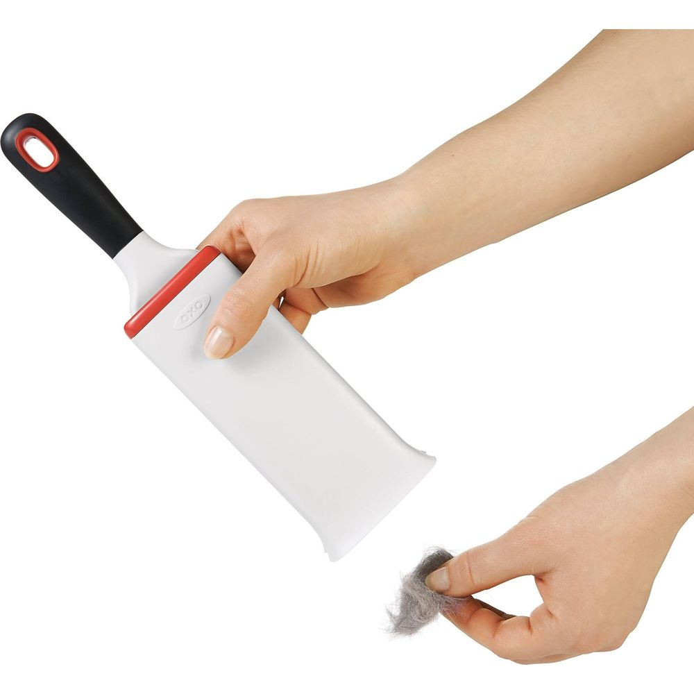 Eine Hand hält einen weißen Fusselbürstenhalter mit schwarzem Griff. Eine andere Hand hält eine graue Staubfluse.