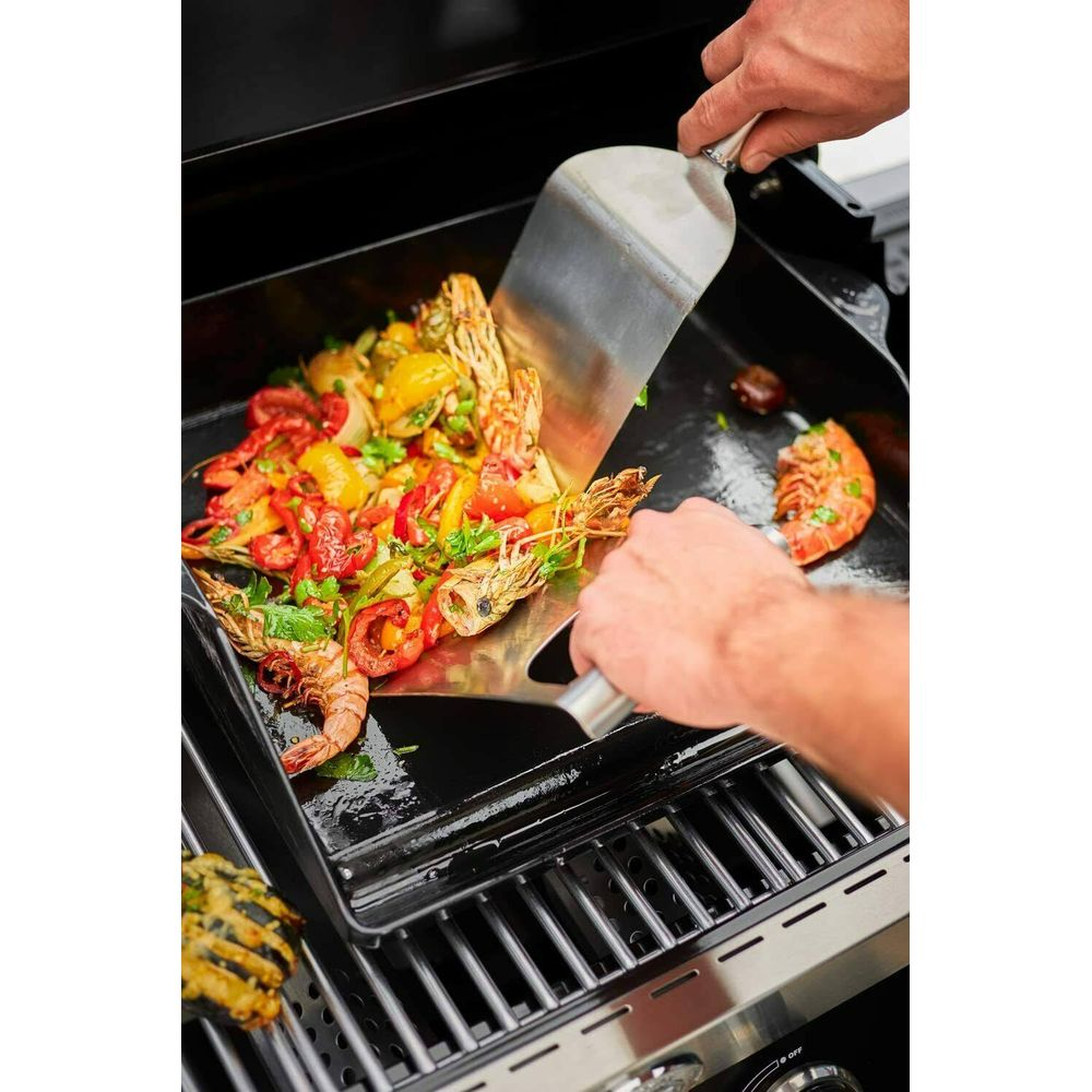 Garnelen und Gemüse werden mit einem Spatel auf einem Grill zubereitet.