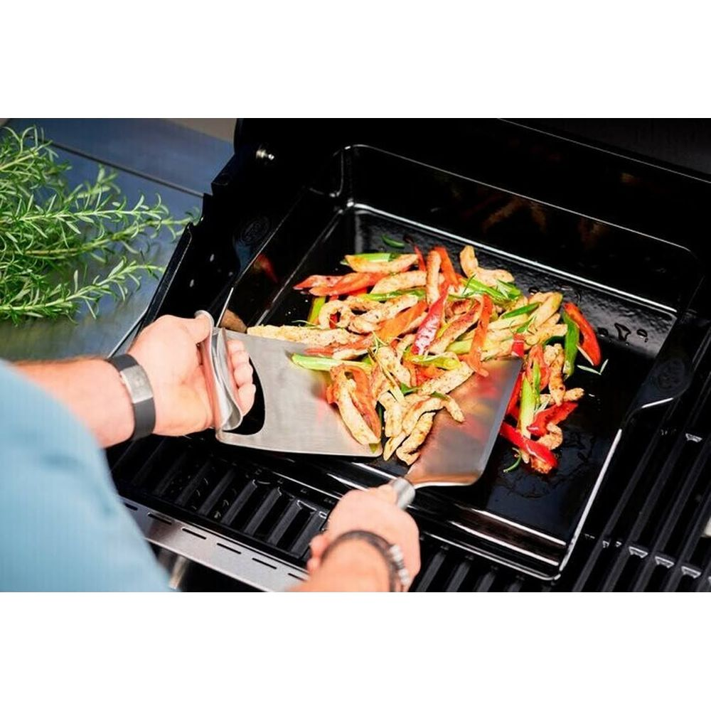 Fleisch und Gemüse wird auf einem Grill mit einem Spatel gewendet.