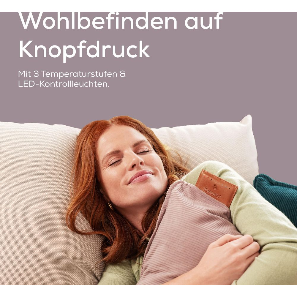 Frau mit roten Haaren entspannt auf einem Sofa, hält eine Wärmflasche.