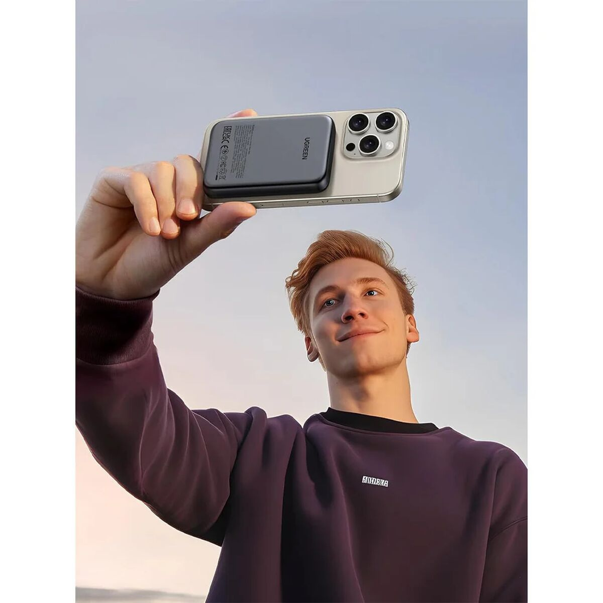 A man holds a smartphone with a charger attached up in the air.