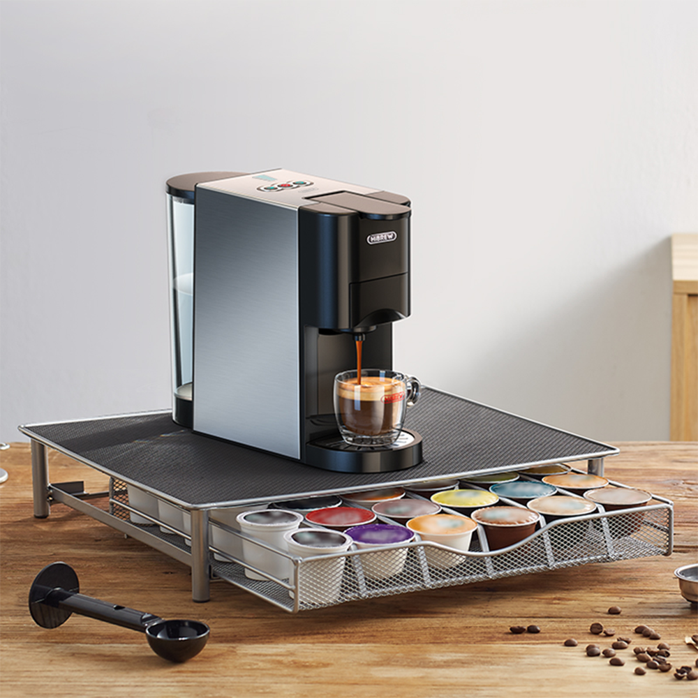 Cafetera preparando espresso en taza de cristal; cajón de cápsulas de café debajo.