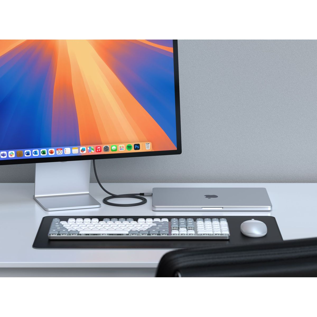 Ein silberner Laptop, Tastatur und Maus auf einem Schreibtisch vor einem großen Monitor.
