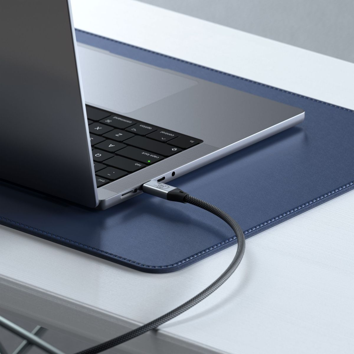 Ein Ladekabel ist in einen silbernen Laptop auf einer blauen Unterlage eingesteckt.