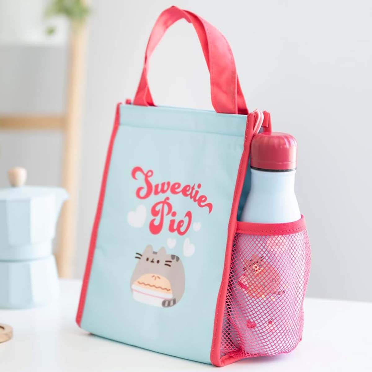 Eine hellblaue Lunchtasche mit pinkfarbenem Besatz und Griffen, mit Cartoon-Katze und Text.