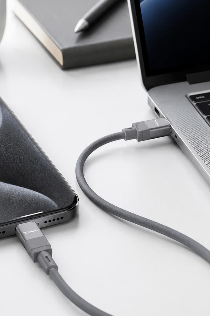 Gri bir USB-C kablosu, akıllı telefonu beyaz bir masadaki dizüstü bilgisayara bağlıyor.