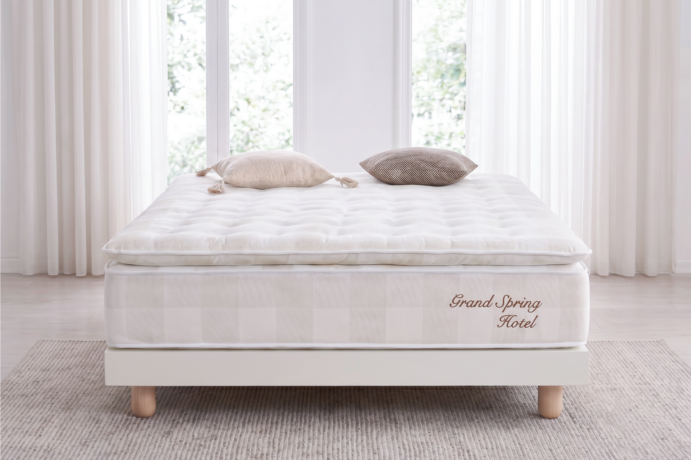 Un colchón blanco con dos almohadas sobre un somier blanco, con cortinas al fondo.